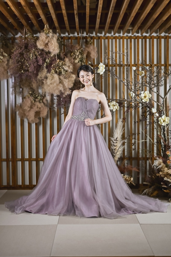 格子とドライフラワーの前に立つ、ビジューのラベンダー色のカラードレスの花嫁の前撮りの衣装写真