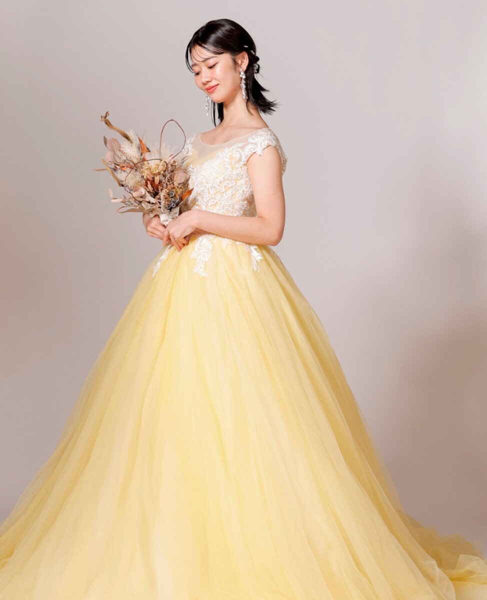 ドライフラワーのブーケを持つ、レースのイエローのカラードレスの花嫁。スタジオフォトの衣装写真
