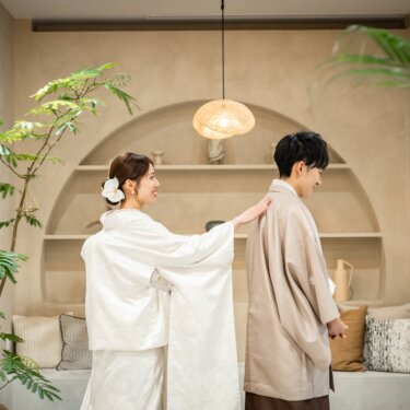 背を向けた羽織袴の新郎の肩に、白無垢の花嫁がそっと手を置くファーストミートの和装スタジオフォト
