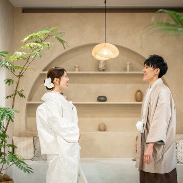 アーチの飾り棚の前で向き合い、笑顔を交わす白無垢の花嫁と羽織袴の新郎。ファーストミートの和装スタジオフォト