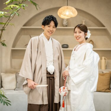 アーチの飾り棚の前に並ぶ、扇子を持つ羽織袴の新郎とはこせこを持つ白無垢の花嫁の和装スタジオフォト