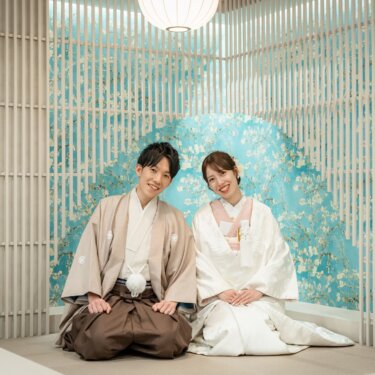格子と花柄の壁の和モダンなセットに正座して笑う、羽織袴の新郎と白無垢の花嫁の和装スタジオフォト