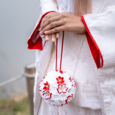 白無垢の花嫁が手にした赤と白の花のまりのような小物と、指輪が光る手元のクローズアップの和装前撮り
