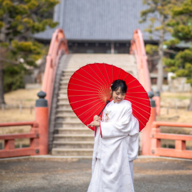 称名寺の反橋と金堂を背に、赤い和傘を差してほほえむ白無垢の花嫁のソロショットの和装前撮り