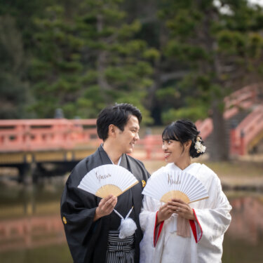 朱色の橋を望む池のほとりで、'Groom''Bride'の扇子を手に見つめ合う新郎新婦の和装前撮り