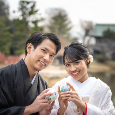 称名寺の池と反橋を背に、色とりどりの手毬を持ってカメラに笑う紋付袴の新郎と白無垢の花嫁の和装フォトウェディング