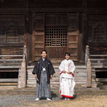 称名寺の歴史ある木造のお堂の前に並んで立つ、白無垢の花嫁と黒紋付袴の新郎の和装前撮り