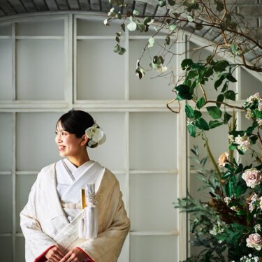 花とグリーンのアーチ窓の前でほほえむ、白い花の髪飾りをつけた白無垢の花嫁のポートレートの和装前撮り