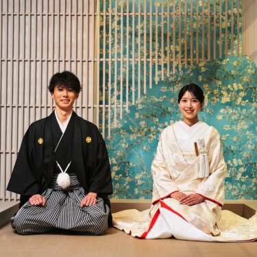 和紙の格子と青緑の花柄壁紙を背に、正座で並ぶ新郎新婦の記念写真。スタジオで撮る和装フォトウェディング