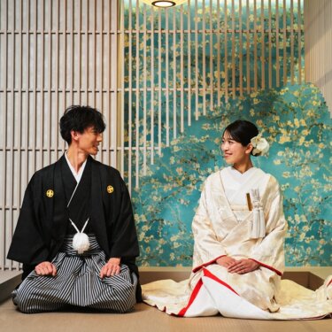 青緑の花柄壁紙と格子のセットで正座し、見つめ合う紋付袴の新郎と白無垢の花嫁。和モダンな和装前撮り