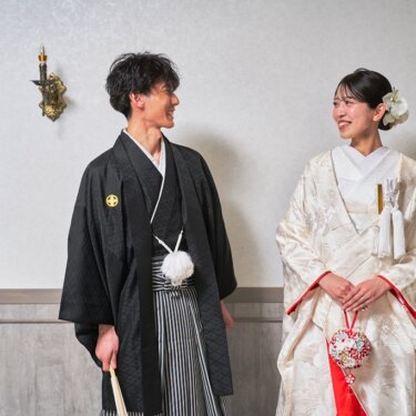 白い花のかんざしと抱え帯が美しい白無垢の花嫁と、扇子を持つ紋付袴の新郎が見つめ合う和装前撮り