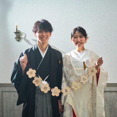 '結婚しました'の木製ガーランドを二人で掲げて笑う紋付袴の新郎と白無垢の花嫁。結婚報告にも使える和装前撮り