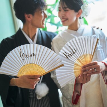 'Groom''Bride'の文字入り扇子を掲げて笑い合う新郎新婦のアップ。小物を使った和装前撮り