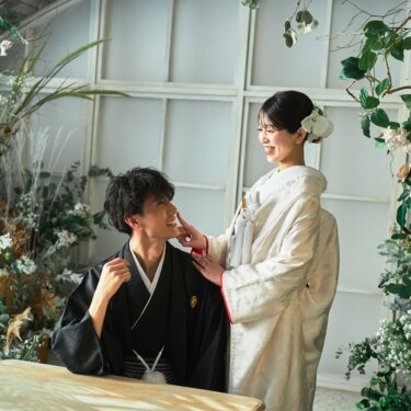 木のテーブルにつく新郎の頬に、白無垢の花嫁がそっと触れるほほえましい和装フォトウェディング