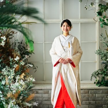 花のアーチ窓の前で、赤い裏地の裾を広げて立つ白無垢の花嫁の全身ショット。和装フォトウェディング