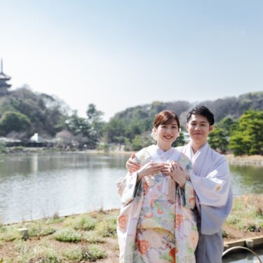 三渓園の大池の向こうに旧燈明寺三重塔を望む、カメラを見つめる和装の新郎新婦を写した雄大な和装前撮り