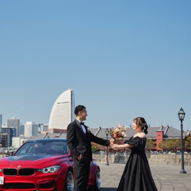 象の鼻パークで赤い愛車を背に、ブーケを渡す新郎とウェディングドレスの花嫁の前撮り