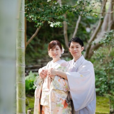 竹の間から、寄り添ってカメラを見つめる新郎新婦を写したのぞき見構図の和装フォトウェディング