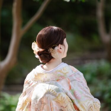 金の髪飾りをつけたまとめ髪と、淡い花柄の色打掛の刺繍を写した花嫁の後ろ姿。和装前撮りのヘアアレンジ
