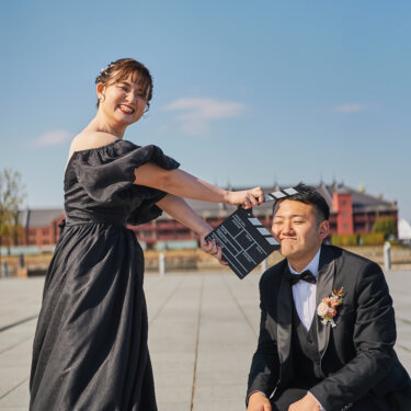 赤レンガ倉庫を望む象の鼻パークで、カチンコを新郎の頭にかざす花嫁の遊び心ある前撮り