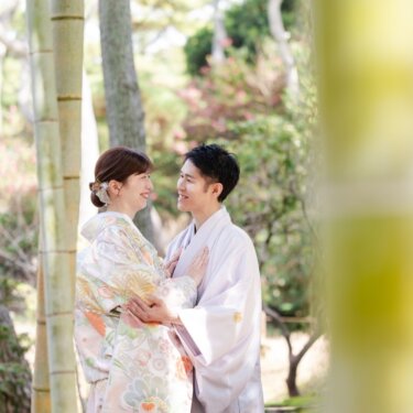 竹林の中で見つめ合って笑う新郎新婦の横顔。竹をぼかした前景がやさしい和装フォトウェディング