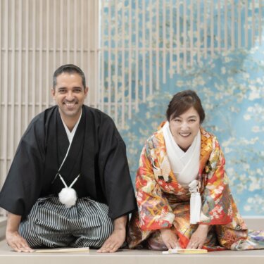 青い花柄の壁と障子格子のセットで並んで正座する、紋付袴の新郎と色打掛の花嫁の和装前撮り
