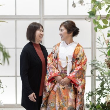 花のアーチ窓のセットで、家族の女性と見つめ合って笑う色打掛の花嫁。家族と一緒のスタジオフォト