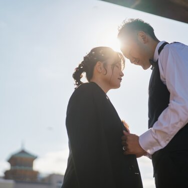 象の鼻パークにて、逆光の太陽を背に額を合わせる新郎新婦。塔の屋根がのぞく横浜の街で撮るシルエットの前撮り