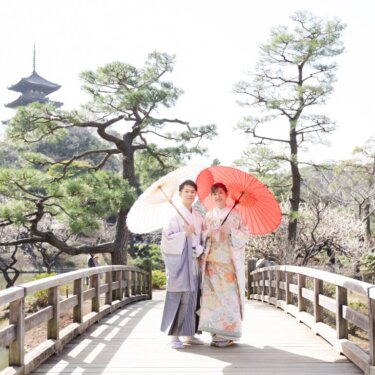 三渓園の旧燈明寺三重塔を望む橋の上で、白と朱赤の和傘を差して立つ新郎新婦の和装前撮り