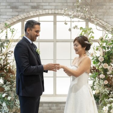 アーチ窓と花に囲まれたセットで、手を取り合って見つめ合う新郎新婦のウェディングフォト