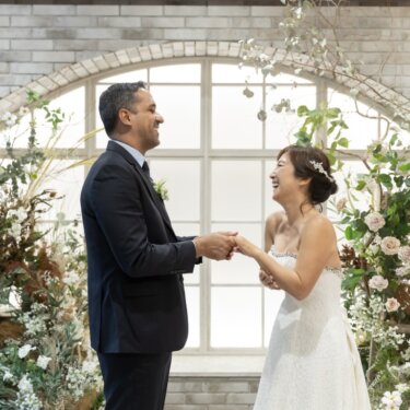 花のアーチ窓のセットで手を取り合い、大笑いする新郎とウェディングドレスの花嫁の結婚写真