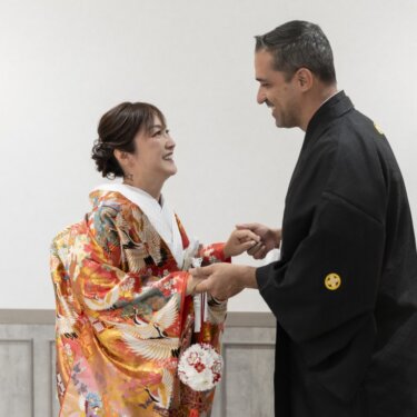 壁灯のある部屋で手を取り合い、笑顔がはじける色打掛の花嫁と新郎。ファーストミートの和装前撮り