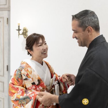 扉の前で手を取り合う色打掛の花嫁と紋付袴の新郎のアップ。ファーストミートの和装フォトウェディング