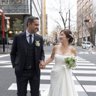 横断歩道を手をつないで渡る新郎新婦。都会の街並みを背景にした街ロケのウェディングフォト