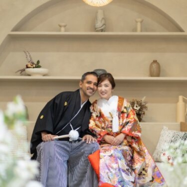 アーチの飾り棚のセットで頭を寄せ合い、カメラに笑う紋付袴の新郎と色打掛の花嫁の和装前撮り