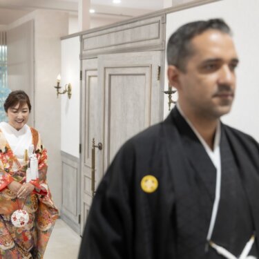 手前の紋付袴の新郎をぼかし、奥からほほえみながら歩いてくる鶴柄の色打掛の花嫁を写した和装フォトウェディング