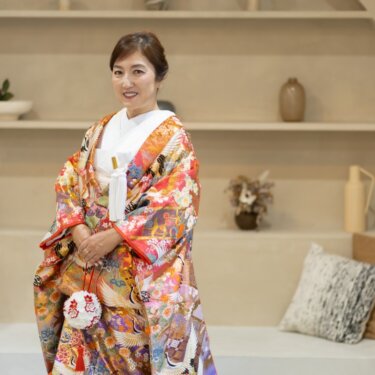 アーチの飾り棚を背に立つ、鶴と花の刺繍が華やかな色打掛の花嫁のソロショット。スタジオの和装前撮り