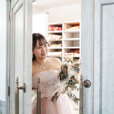 衣装室の大きな扉から顔を出す、ピンクのカラードレスの花嫁。ファーストミートの演出で撮るスタジオフォト