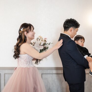 スタジオの壁灯を背に、息子を抱く新郎の背中に花嫁が手を添える家族3人の家族写真入りのスタジオフォト