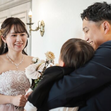 息子を抱きしめる新郎と、見守って笑うピンクのカラードレスの花嫁。家族で撮るフォトウェディング