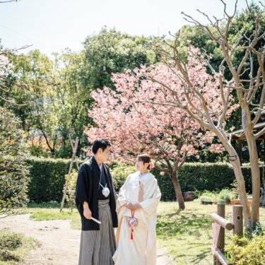 横溝屋敷の桜の咲く小道に並んで立つ新郎新婦を、青空とともに写した春の和装フォトウェディング