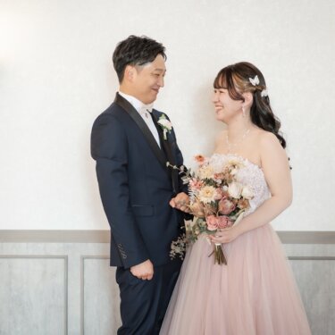 壁灯のある白い壁の前で向かい合って笑う新郎とピンクのカラードレスの花嫁のスタジオフォト