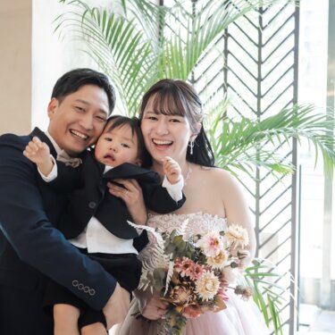観葉植物とアイアン装飾の窓を背に、息子を抱いて大笑いする家族3人のフォトウェディング
