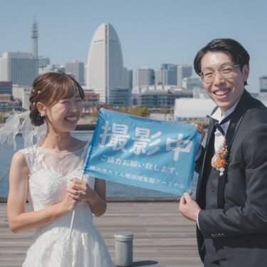 大さん橋の撮影許可の旗を一緒に持って大笑いする、タキシードの新郎とウェディングドレスの花嫁のロケーションフォト