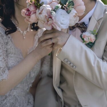 ピンクのブーケで顔を隠すように寄り添う新郎新婦のアップ。指輪が光る手元も写る遊び心ある前撮り