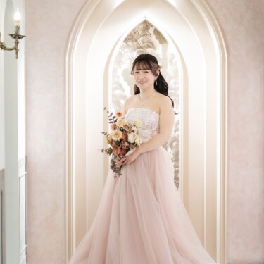 ゴシック調のアーチ型ニッチを背景に、ピンクのカラードレス姿の花嫁のソロショット。フォトウェディングの一枚