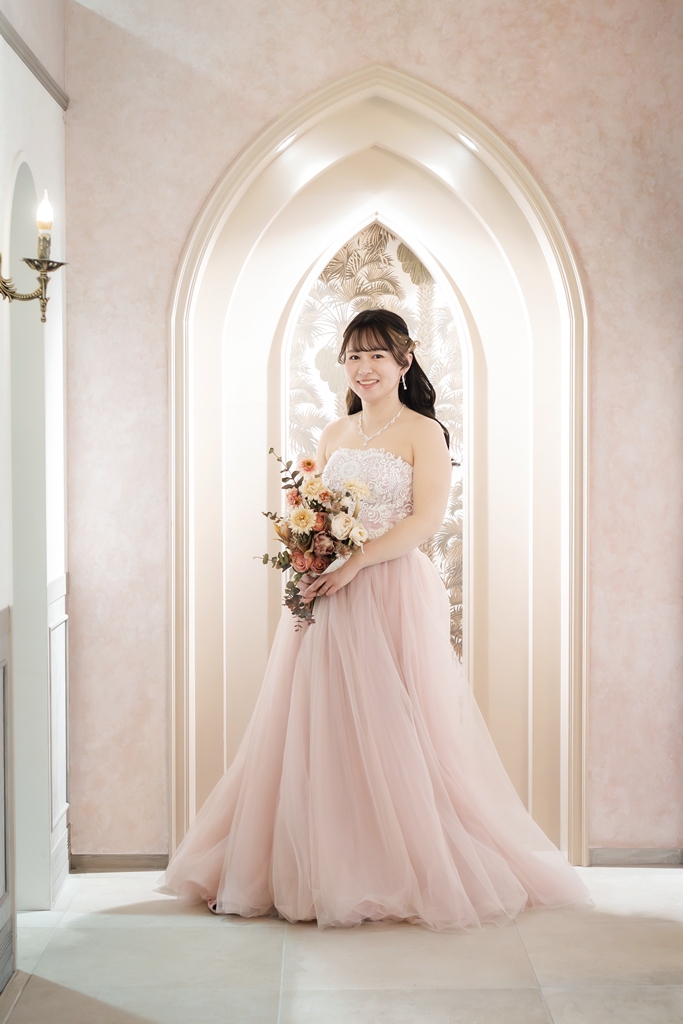 ゴシック調のアーチ型ニッチを背景に、ピンクのカラードレス姿の花嫁のソロショット。フォトウェディングの一枚