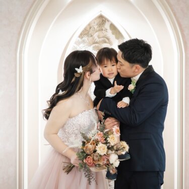 ゴシック調のアーチのセットで、両親がそれぞれ息子のほおにキスをする家族3人のスタジオフォト