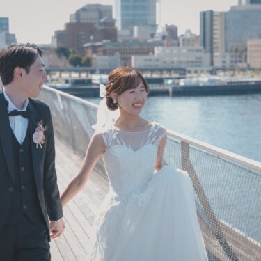 大さん橋のウッドデッキを手をつないで歩き、笑い合う新郎新婦。港と横浜の街並みが広がるウェディングフォト