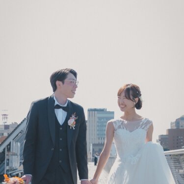大さん橋のデッキを手をつないで歩き、笑顔を交わす新郎新婦。明るい空を広く入れたウェディングフォト